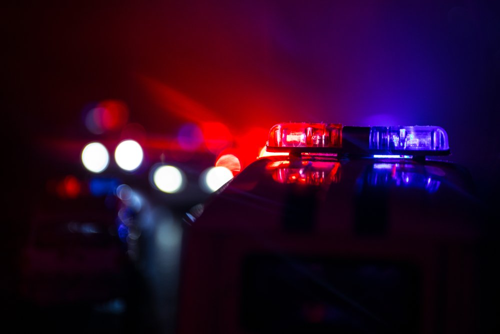 Flashing red and blue police car lights are visible in the foreground