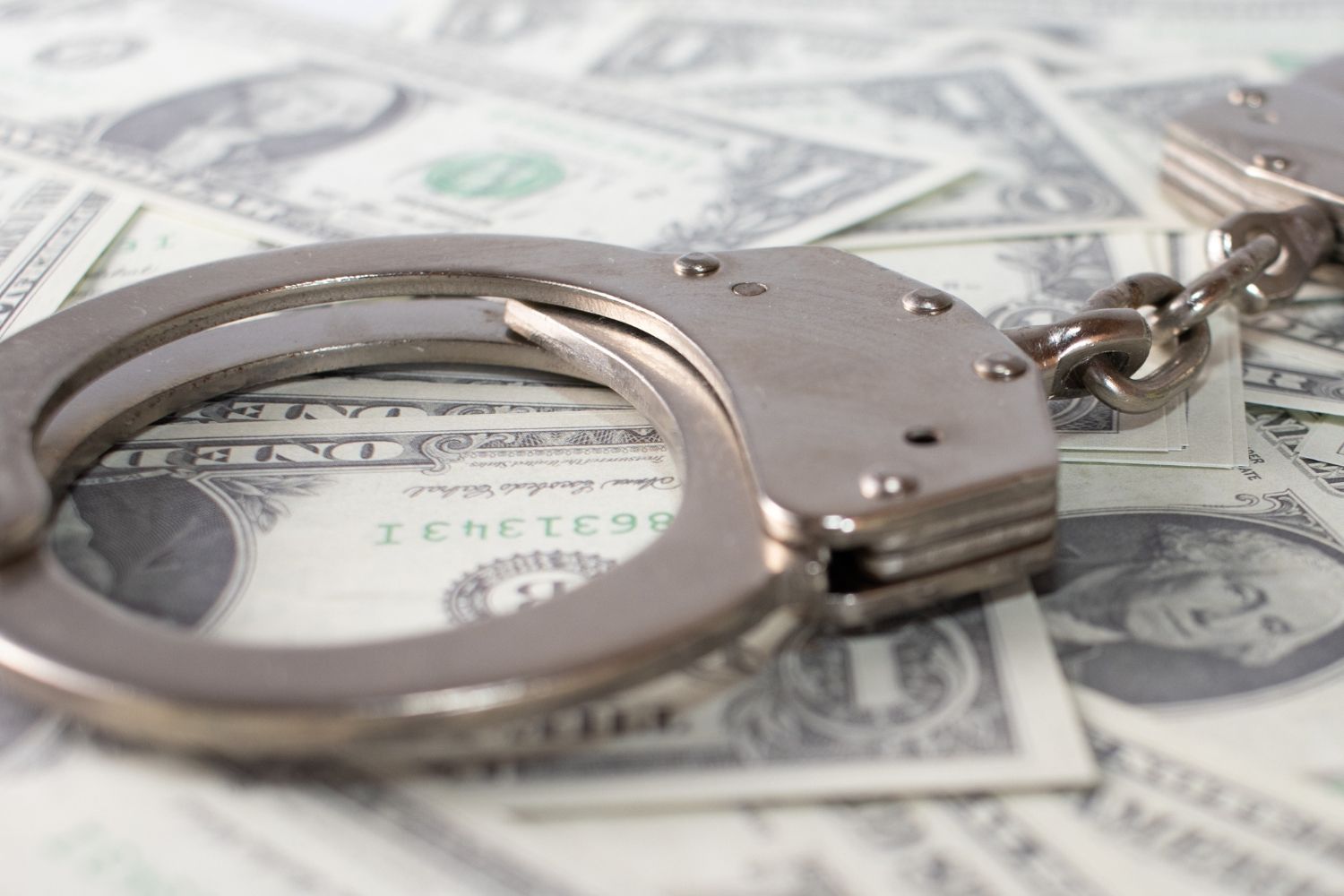 Silver handcuffs rest on a scattered pile of dollar bills
