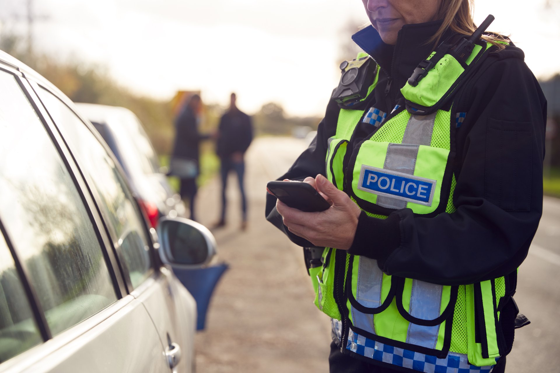 A police officer in a high-visibility vest with "POLICE" written on it holds a device.