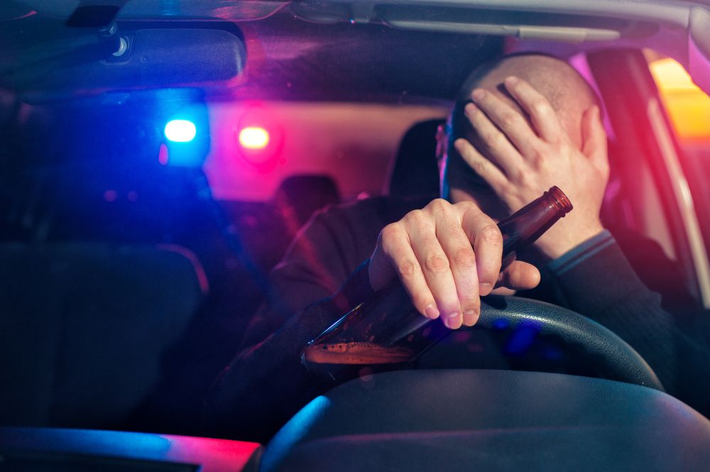 A distressed man holds an alcohol bottle in a car