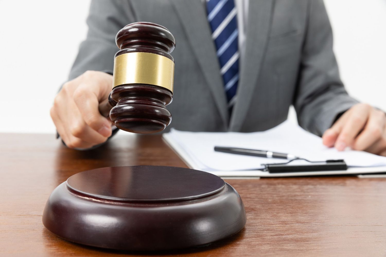 A person in a suit holds a gavel poised above a sound block on a wooden desk