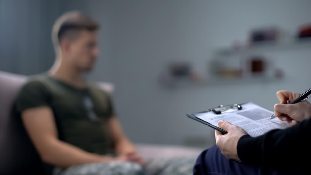A therapist's hands write on a clipboard in the foreground
