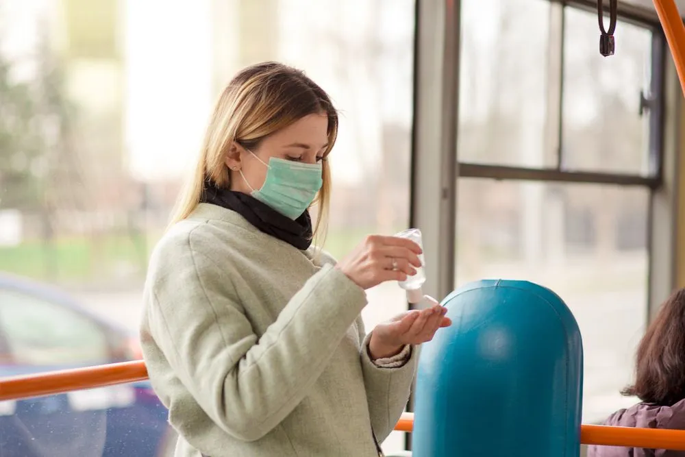 A masked woman applies hand sanitizer while riding public transport
