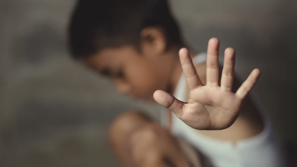 A blurred image shows a young child with an outstretched hand, palm forward, in a defensive "stop" gesture.